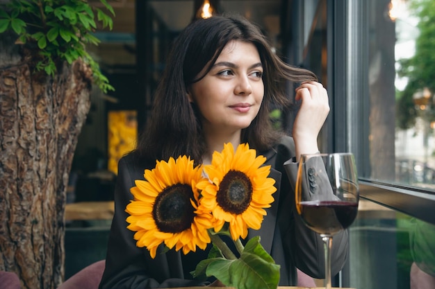 Una mujer joven con una copa de vino y un ramo de girasoles en un restaurante.