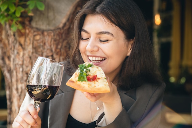 Una mujer joven con una copa de vino y un trozo de pizza en un restaurante.