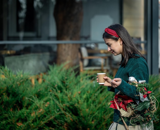 Mujer joven con una corona de Navidad y una taza de café en un paseo por la ciudad