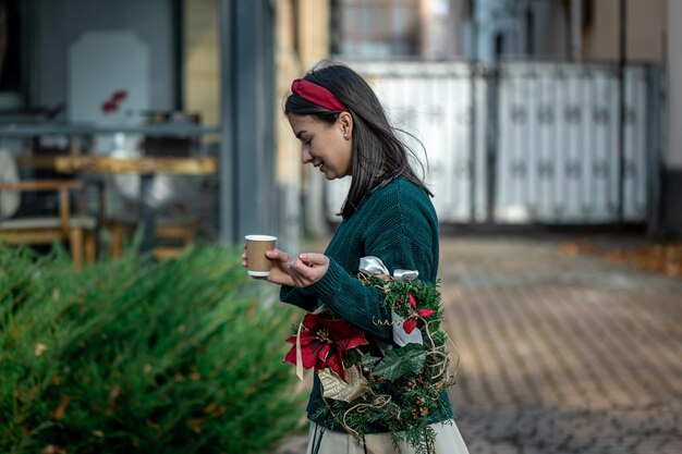 Mujer joven con una corona de Navidad y una taza de café en un paseo por la ciudad