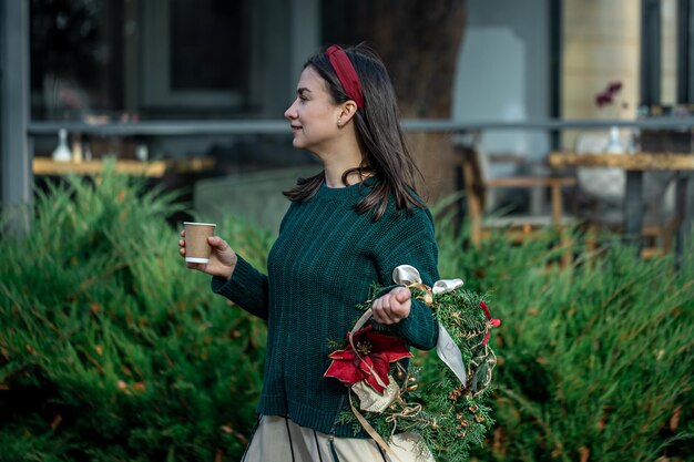 Mujer joven con una corona de Navidad y una taza de café en un paseo por la ciudad