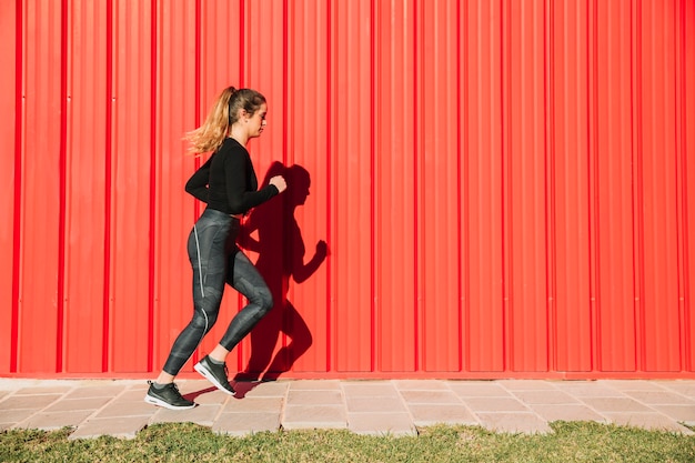 Foto gratuita mujer joven corriendo cerca de la pared roja