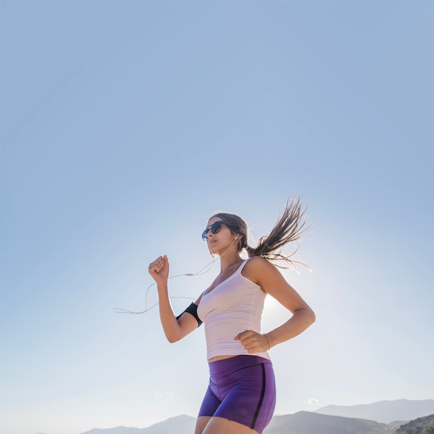 Mujer joven corriendo con el cielo azul de fondo