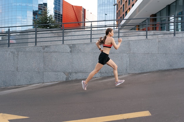 Mujer joven corriendo por la mañana al aire libre. Vista lateral de la corredora trabajando en la ciudad.
