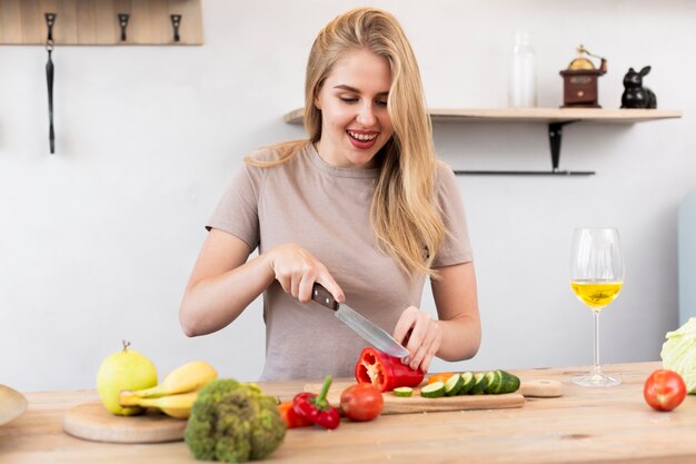 Mujer joven cortando el pimiento en la cocina