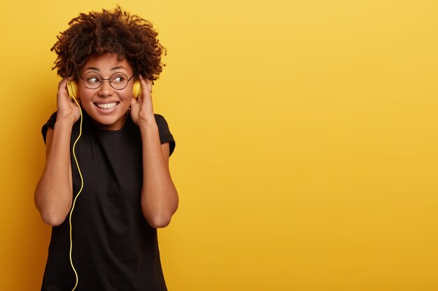 Mujer joven con corte de pelo afro y auriculares amarillos