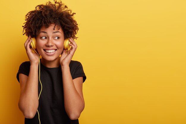 Mujer joven con corte de pelo afro y auriculares amarillos