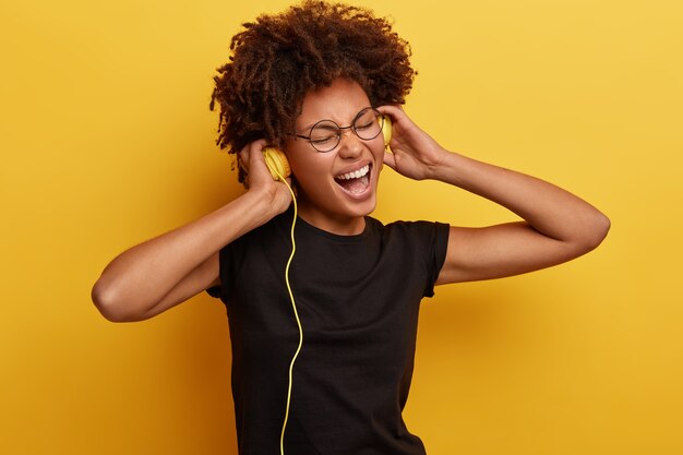 Mujer joven con corte de pelo afro con auriculares amarillos