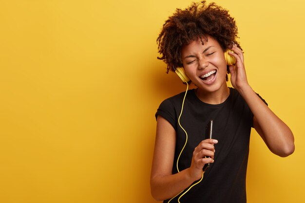 Mujer joven con corte de pelo afro con auriculares amarillos