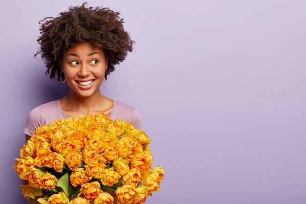 Mujer joven con corte de pelo afro con ramo de flores amarillas