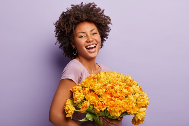 Mujer joven con corte de pelo afro con ramo de flores amarillas