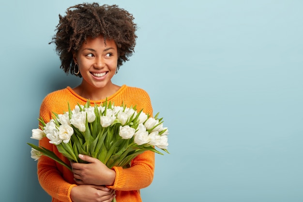 Mujer joven con corte de pelo afro con ramo de flores blancas