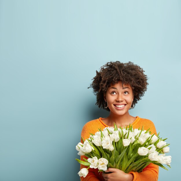 Mujer joven con corte de pelo afro con ramo de flores blancas