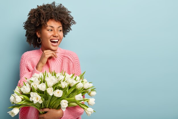 Mujer joven con corte de pelo afro con ramo de flores blancas