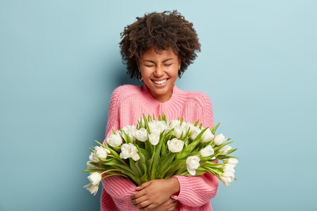 Mujer joven con corte de pelo afro con ramo de flores blancas