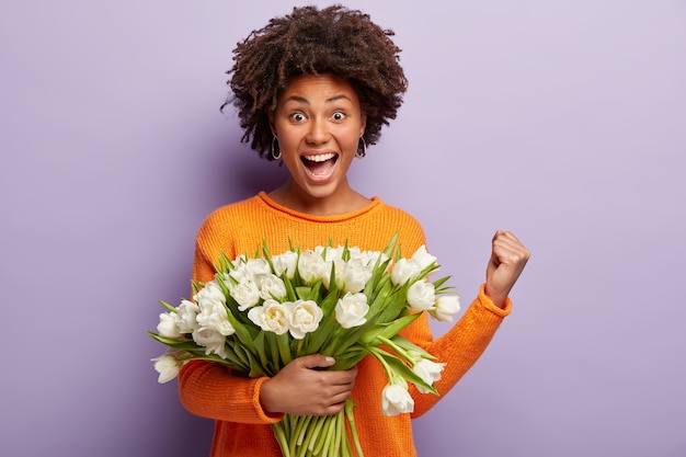 Mujer joven con corte de pelo afro con ramo de flores blancas