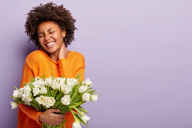 Mujer joven con corte de pelo afro con ramo de flores blancas