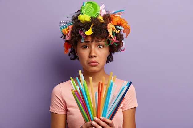 Mujer joven con corte de pelo afro y residuos plásticos en el cabello