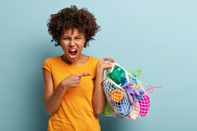 Mujer joven con corte de pelo afro sosteniendo la bolsa con residuos plásticos