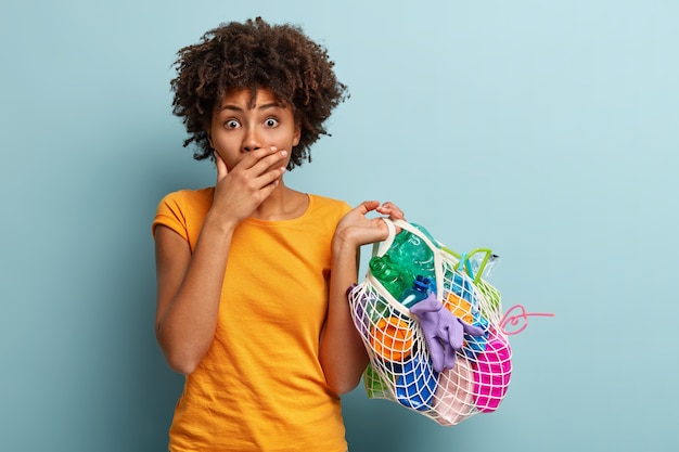 Mujer joven con corte de pelo afro sosteniendo la bolsa con residuos plásticos