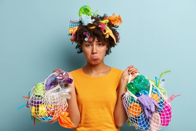 Mujer joven con corte de pelo afro sosteniendo la bolsa con residuos plásticos