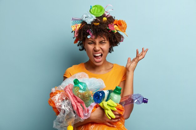 Mujer joven con corte de pelo afro sosteniendo la bolsa con residuos plásticos