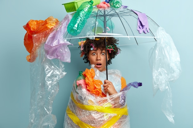 Mujer joven con corte de pelo afro sosteniendo la bolsa con residuos plásticos