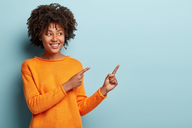 Mujer joven con corte de pelo afro vistiendo jersey naranja