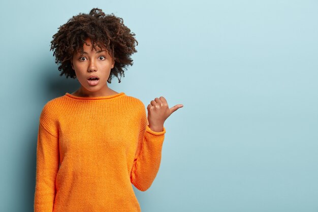 Mujer joven con corte de pelo afro vistiendo jersey naranja