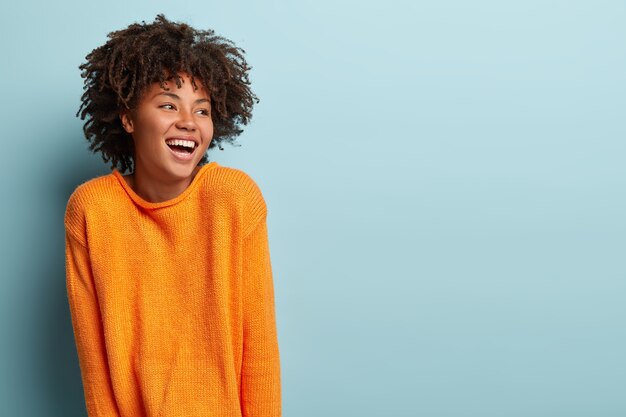 Mujer joven con corte de pelo afro vistiendo jersey naranja