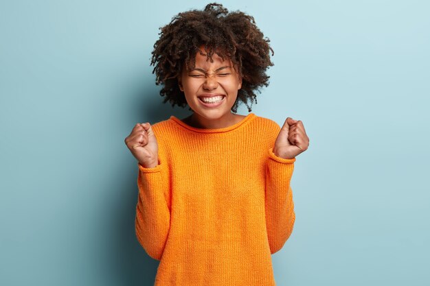 Mujer joven con corte de pelo afro vistiendo suéter naranja