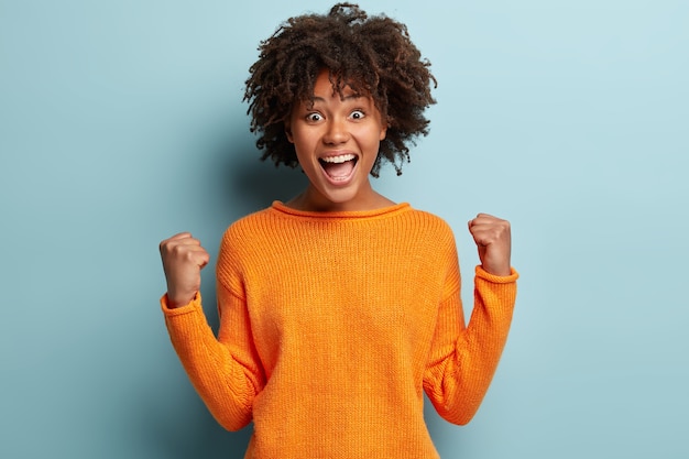 Mujer joven con corte de pelo afro vistiendo suéter naranja