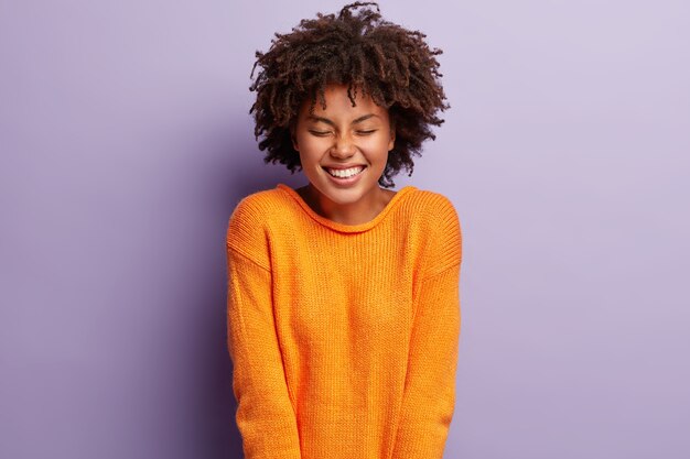 Mujer joven con corte de pelo afro vistiendo suéter naranja