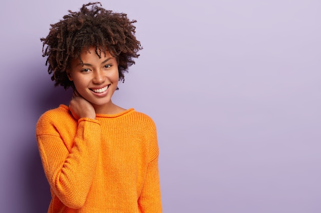 Mujer joven con corte de pelo afro vistiendo suéter naranja