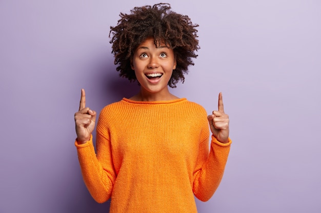 Mujer joven con corte de pelo afro vistiendo suéter naranja