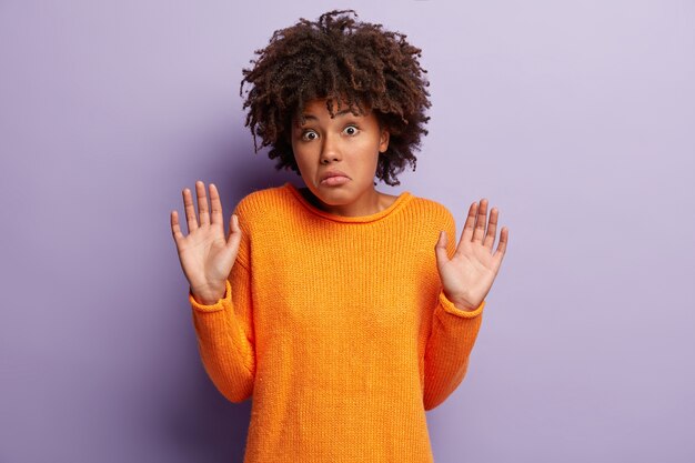 Mujer joven con corte de pelo afro vistiendo suéter naranja