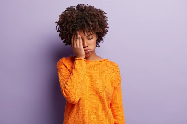 Mujer joven con corte de pelo afro vistiendo suéter naranja
