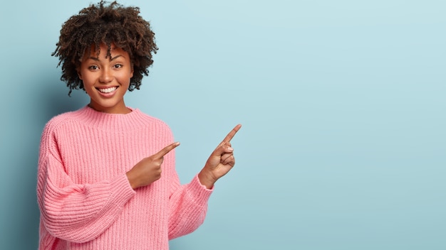 Mujer joven con corte de pelo afro vistiendo suéter rosa