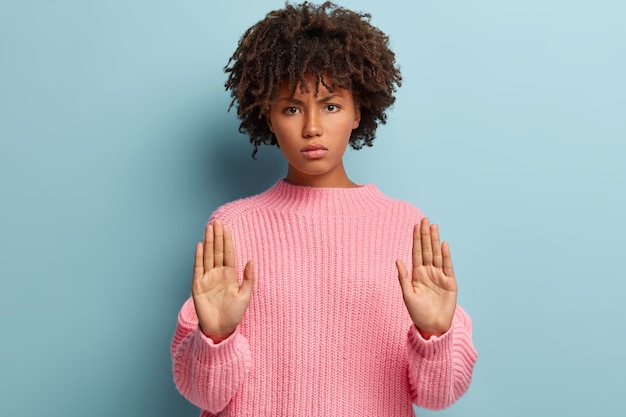 Mujer joven con corte de pelo afro vistiendo suéter rosa