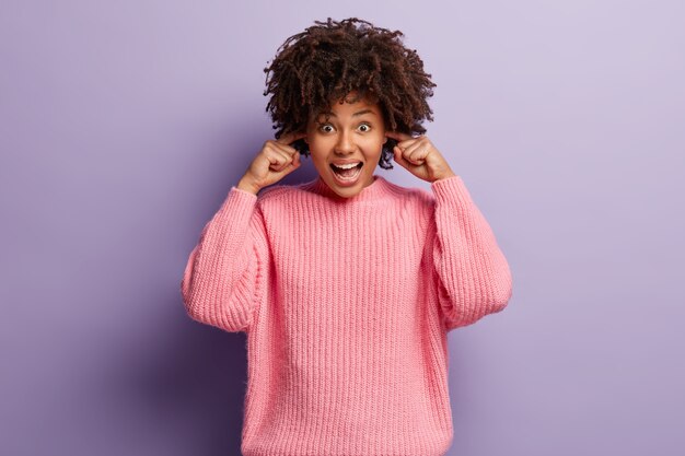 Mujer joven con corte de pelo afro vistiendo suéter rosa