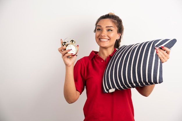 Foto gratuita mujer joven en corto rojo mostrando un despertador y sosteniendo una almohada.