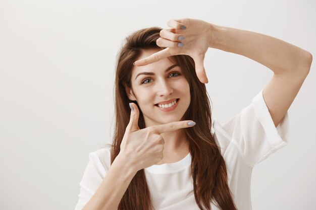 Mujer joven creativa haciendo gesto de captura, imaginando la escena y sonriendo complacido