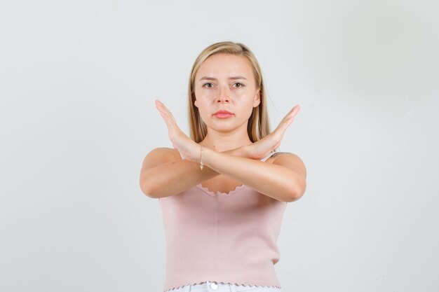 Mujer joven cruzando los brazos haciendo signo negativo en camiseta, minifalda y mirando serio