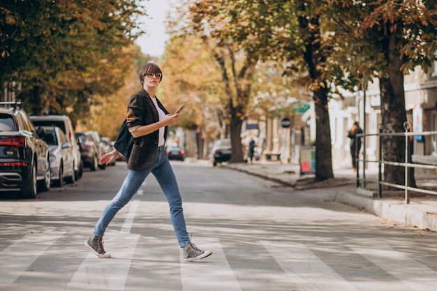 Mujer joven, cruzar la calle, y, utilizar, teléfono