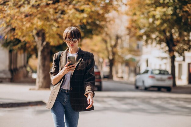 Mujer joven, cruzar la calle, y, utilizar, teléfono