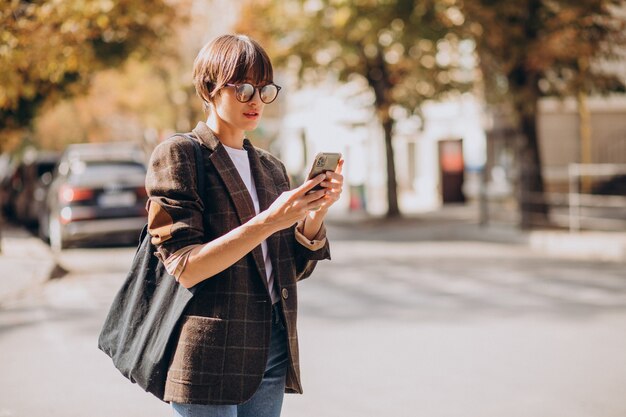 Mujer joven, cruzar la calle, y, utilizar, teléfono