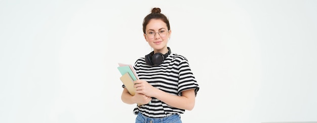 Foto gratuita mujer joven con cuadernos, libros y material de estudio posando sobre fondo blanco usa auriculares