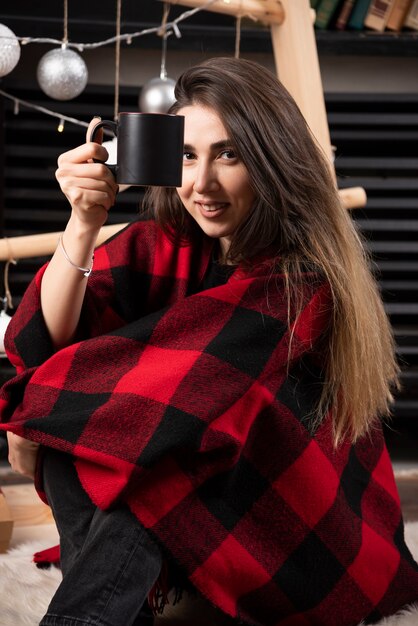 Mujer joven en cuadros escoceses sosteniendo una taza caliente.