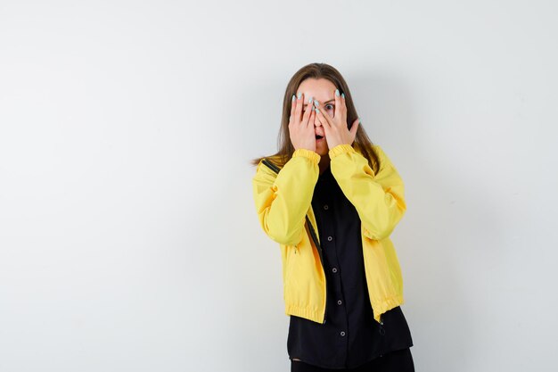 Foto gratuita mujer joven cubriendo los ojos con las manos y mirando a través de los dedos