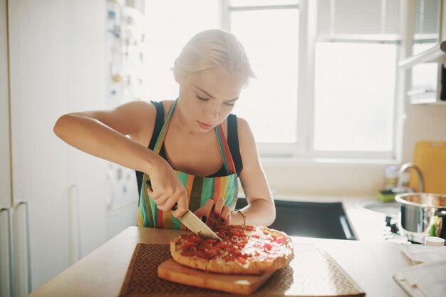 Mujer joven con un cuchillo corta la pizza